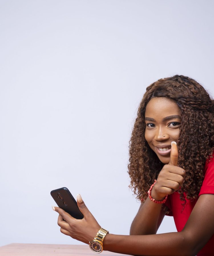 A beautiful black woman sitting sideways, holding her phone and a thumbs up